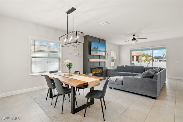 tiled dining area with a fireplace, a wealth of natural light, and ceiling fan with notable chandelier