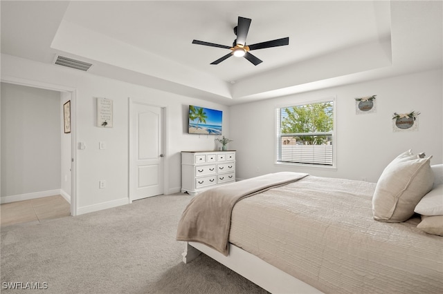 carpeted bedroom with ceiling fan and a raised ceiling