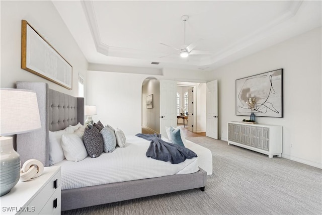 bedroom with light carpet, ceiling fan, and a raised ceiling