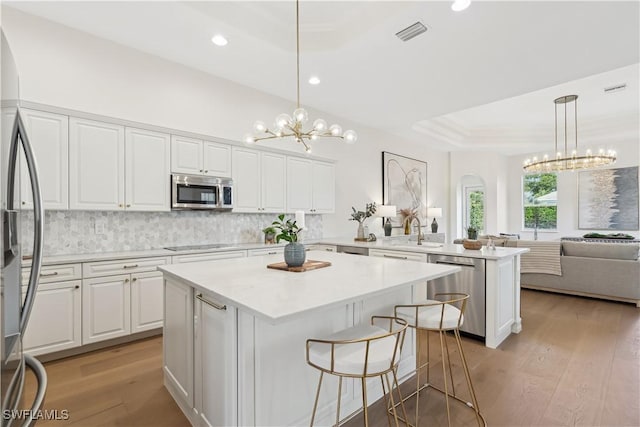 kitchen featuring a center island, appliances with stainless steel finishes, white cabinets, a raised ceiling, and pendant lighting