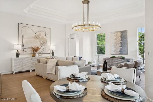 dining room with light wood-style floors, arched walkways, a raised ceiling, and an inviting chandelier