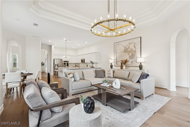 living room with light wood-type flooring, an inviting chandelier, and a tray ceiling