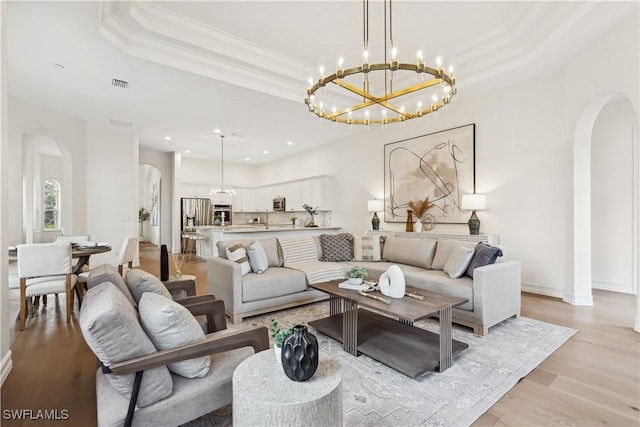 677 5th Ave N, Naples, FL 34102 - living room with arched walkways, a raised ceiling, light wood-style floors, ornamental molding, and a chandelier