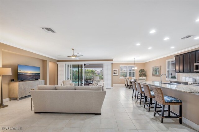 living room featuring ceiling fan, sink, light tile patterned floors, and crown molding