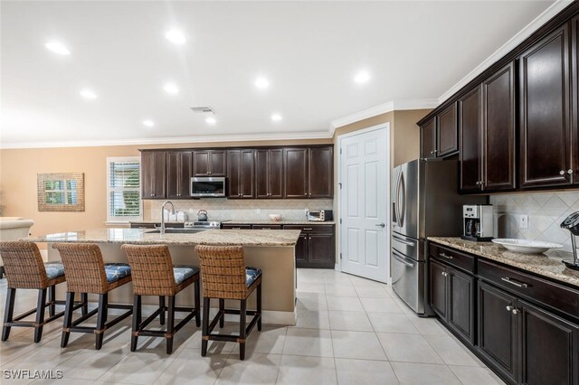 kitchen featuring appliances with stainless steel finishes, light stone countertops, a kitchen island with sink, a kitchen bar, and a sink