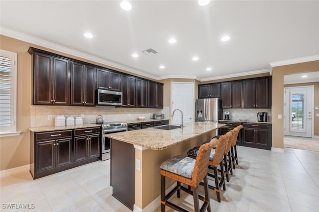 kitchen featuring appliances with stainless steel finishes, sink, a kitchen breakfast bar, a kitchen island with sink, and dark brown cabinets