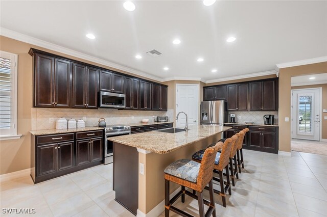 kitchen featuring a kitchen island with sink, stainless steel appliances, a breakfast bar, a sink, and visible vents