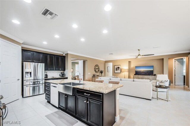 kitchen with crown molding, stainless steel refrigerator with ice dispenser, sink, tasteful backsplash, and a kitchen island with sink