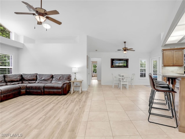 living room with ceiling fan, a wealth of natural light, light tile patterned floors, and lofted ceiling