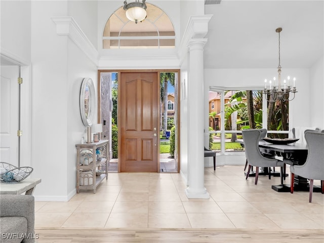 tiled foyer entrance featuring a towering ceiling, decorative columns, plenty of natural light, and a notable chandelier