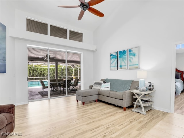 living room with ceiling fan, light hardwood / wood-style floors, and a towering ceiling