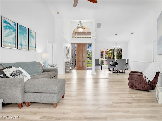 living room with light hardwood / wood-style floors, ceiling fan with notable chandelier, and a towering ceiling