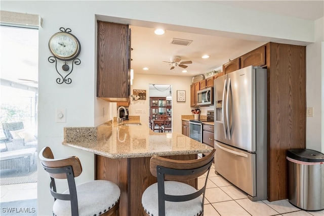 kitchen featuring sink, a kitchen breakfast bar, stainless steel appliances, light stone countertops, and kitchen peninsula