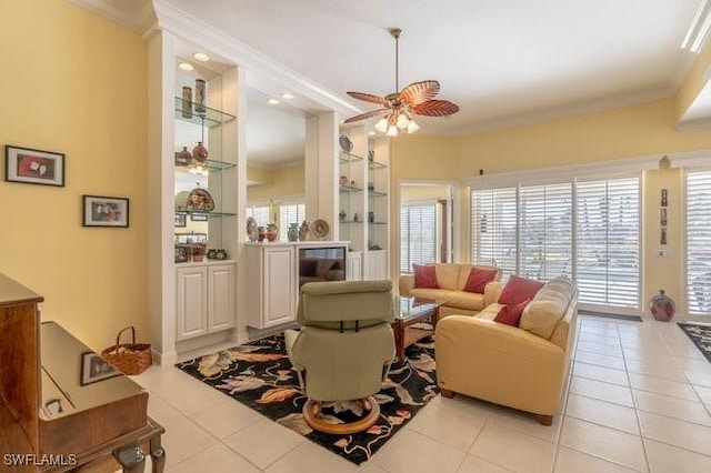 living room featuring ceiling fan, built in shelves, crown molding, and light tile patterned floors