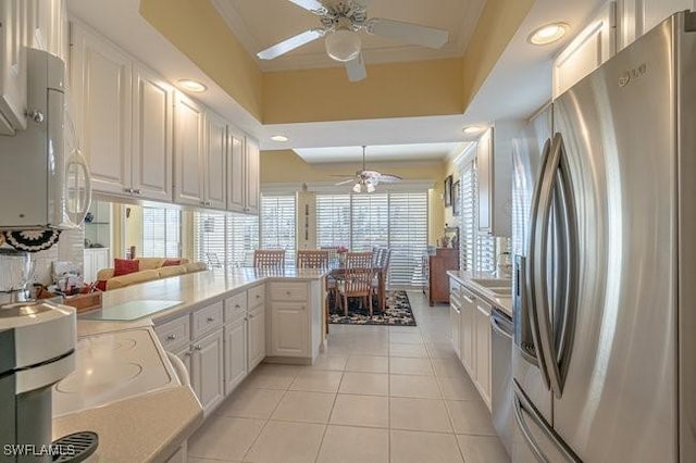 kitchen featuring a raised ceiling, kitchen peninsula, light tile patterned floors, appliances with stainless steel finishes, and white cabinets