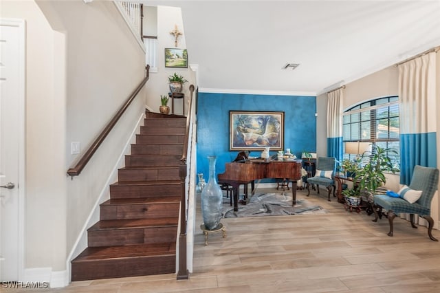 staircase with arched walkways, wood finished floors, visible vents, baseboards, and ornamental molding