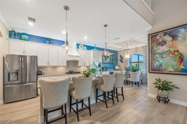 kitchen with appliances with stainless steel finishes, white cabinetry, hanging light fixtures, and a kitchen island with sink