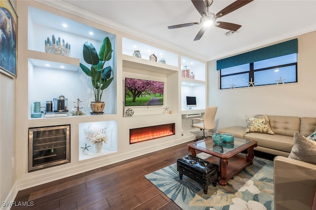 living area featuring a lit fireplace, built in shelves, ornamental molding, and dark wood-style flooring