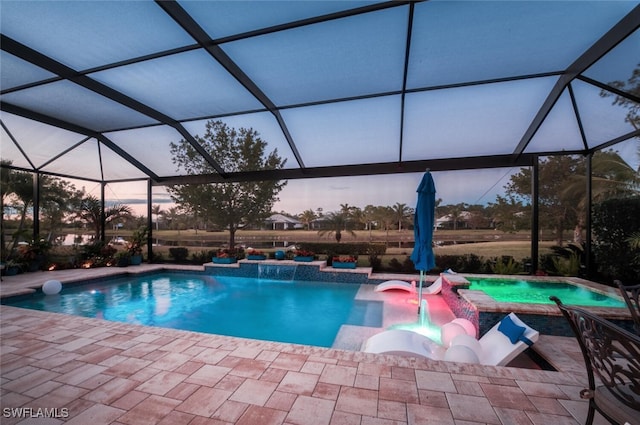 pool at dusk with pool water feature, glass enclosure, a patio area, and a jacuzzi