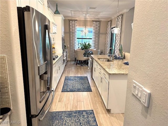 kitchen featuring appliances with stainless steel finishes, light stone counters, ornamental molding, white cabinetry, and pendant lighting