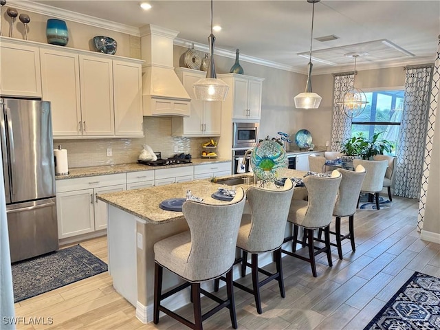 kitchen with pendant lighting, stainless steel appliances, white cabinetry, an island with sink, and light stone countertops