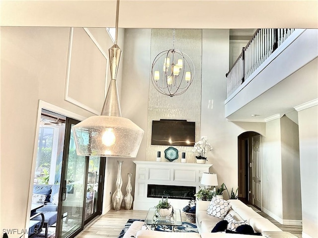 living area featuring arched walkways, a high ceiling, a glass covered fireplace, light wood-type flooring, and baseboards