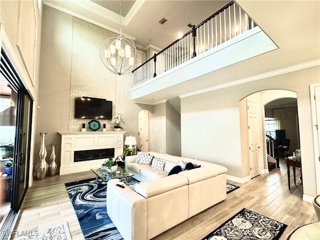 living room featuring arched walkways, a notable chandelier, crown molding, light wood finished floors, and a fireplace