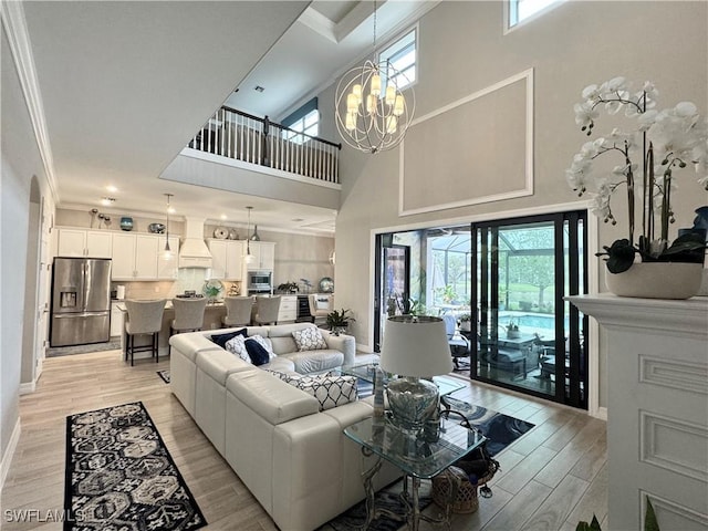 living room featuring light wood-style flooring, a chandelier, baseboards, and ornamental molding