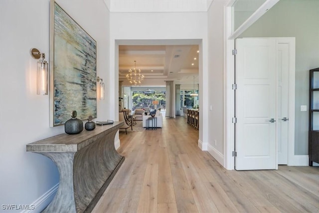 hallway with coffered ceiling, a chandelier, light hardwood / wood-style flooring, and beamed ceiling