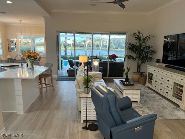 living room featuring ornamental molding, light hardwood / wood-style floors, ceiling fan with notable chandelier, and sink