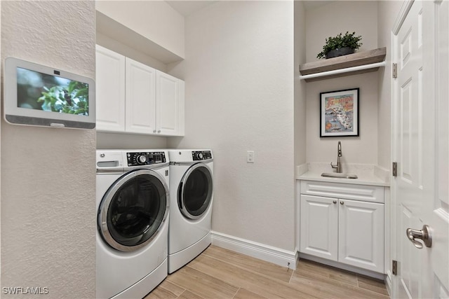 clothes washing area featuring separate washer and dryer, a sink, baseboards, light wood-style floors, and cabinet space