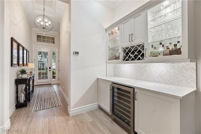 bar featuring tasteful backsplash, an inviting chandelier, hanging light fixtures, ornamental molding, and beverage cooler