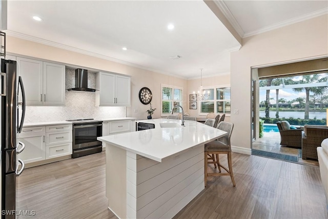 kitchen with freestanding refrigerator, range with electric stovetop, light wood-style flooring, and wall chimney exhaust hood