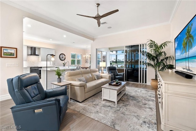 living area with crown molding, visible vents, light wood-style flooring, baseboards, and ceiling fan with notable chandelier