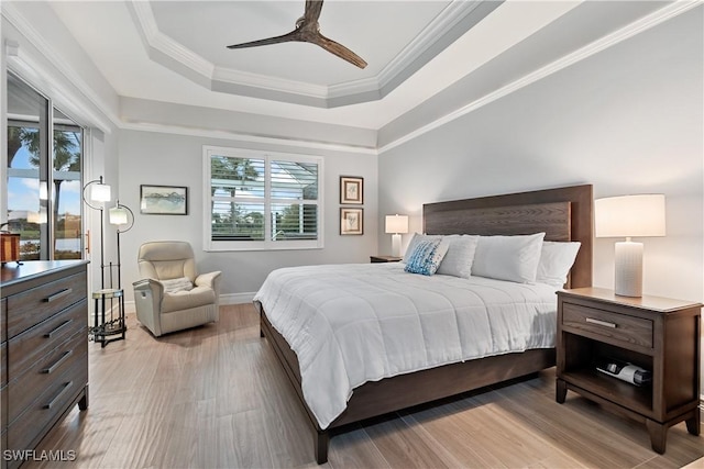 bedroom featuring ceiling fan, baseboards, ornamental molding, a tray ceiling, and light wood finished floors