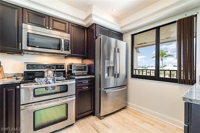 kitchen featuring stainless steel appliances, light hardwood / wood-style floors, dark brown cabinets, and light stone countertops