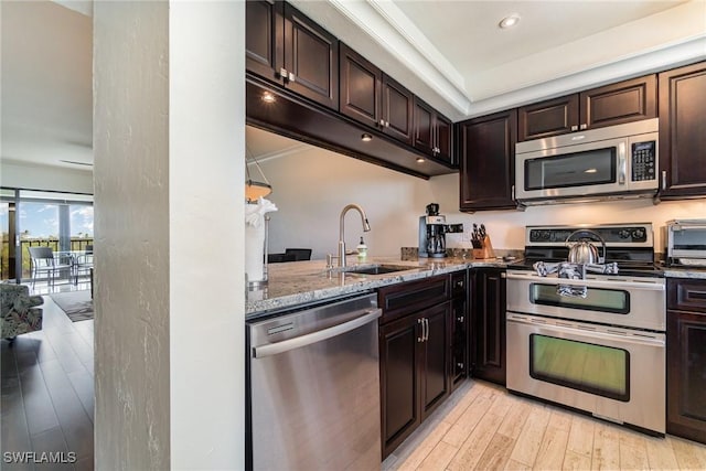 kitchen with appliances with stainless steel finishes, light hardwood / wood-style floors, sink, stone countertops, and dark brown cabinets