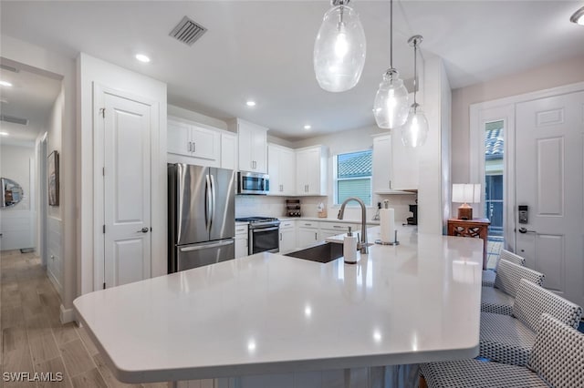 kitchen with pendant lighting, appliances with stainless steel finishes, a kitchen bar, white cabinetry, and sink