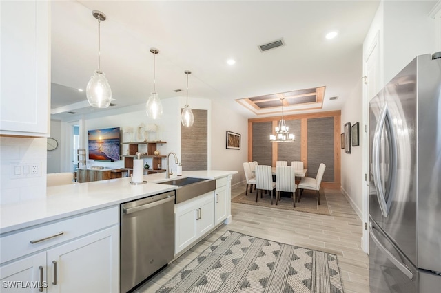 kitchen with decorative light fixtures, white cabinetry, a tray ceiling, and stainless steel appliances