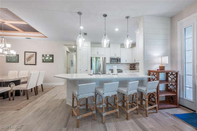 kitchen with white cabinets, stainless steel appliances, an island with sink, a kitchen breakfast bar, and hanging light fixtures