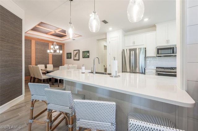 kitchen with pendant lighting, appliances with stainless steel finishes, white cabinetry, sink, and a breakfast bar area