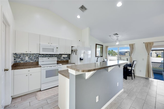 kitchen featuring an island with sink, tasteful backsplash, white appliances, lofted ceiling, and white cabinets