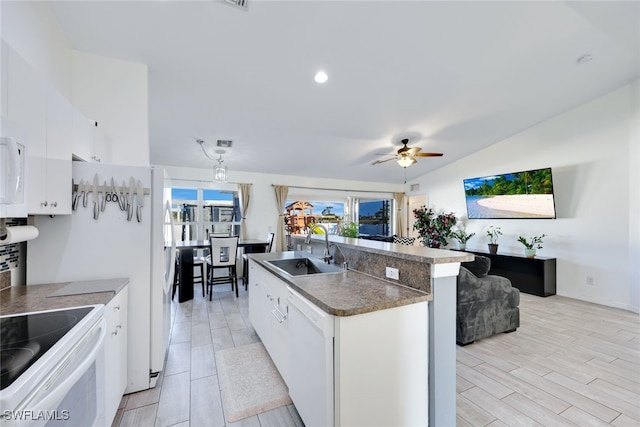 kitchen featuring sink, white appliances, white cabinets, and a center island with sink