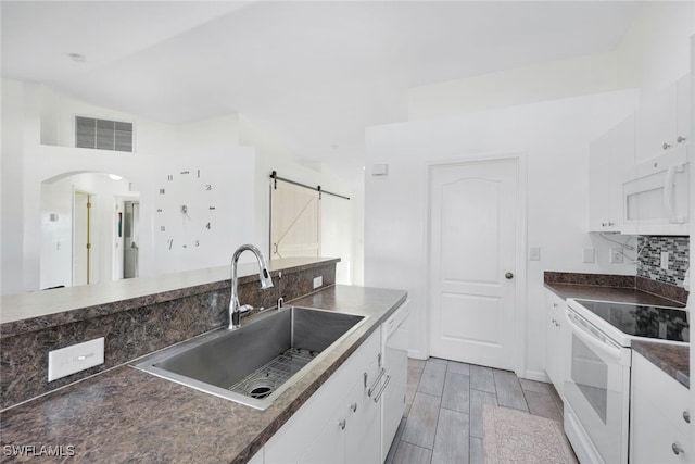 kitchen featuring lofted ceiling, a barn door, sink, white appliances, and white cabinetry