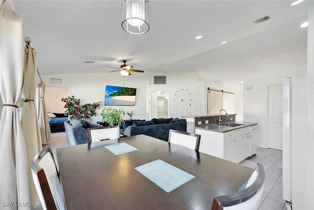 dining space featuring ceiling fan, lofted ceiling, a barn door, and sink