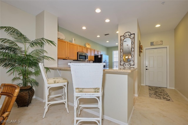 kitchen with light tile patterned floors, a kitchen bar, kitchen peninsula, appliances with stainless steel finishes, and light stone counters