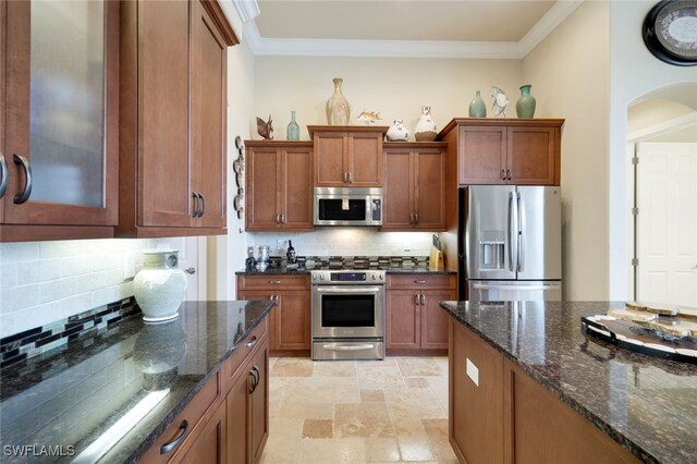 kitchen featuring decorative backsplash, crown molding, stainless steel appliances, and dark stone counters