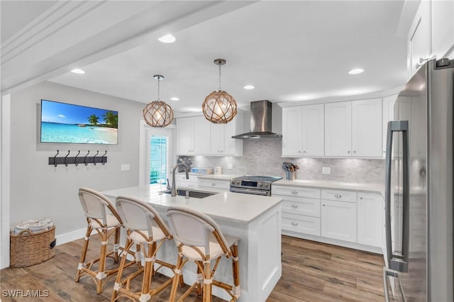 kitchen featuring decorative light fixtures, wall chimney range hood, sink, stainless steel appliances, and white cabinets