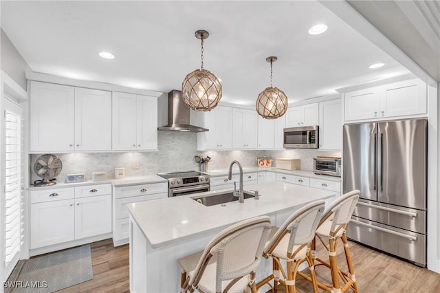 kitchen featuring sink, hanging light fixtures, stainless steel appliances, a center island with sink, and wall chimney range hood