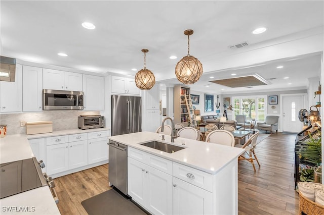 kitchen featuring pendant lighting, white cabinetry, stainless steel appliances, sink, and light hardwood / wood-style flooring